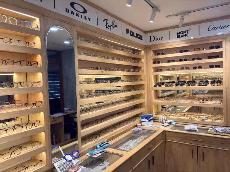Spectacle frames and sunglasses displayed along wooden shelves inside the optical shop